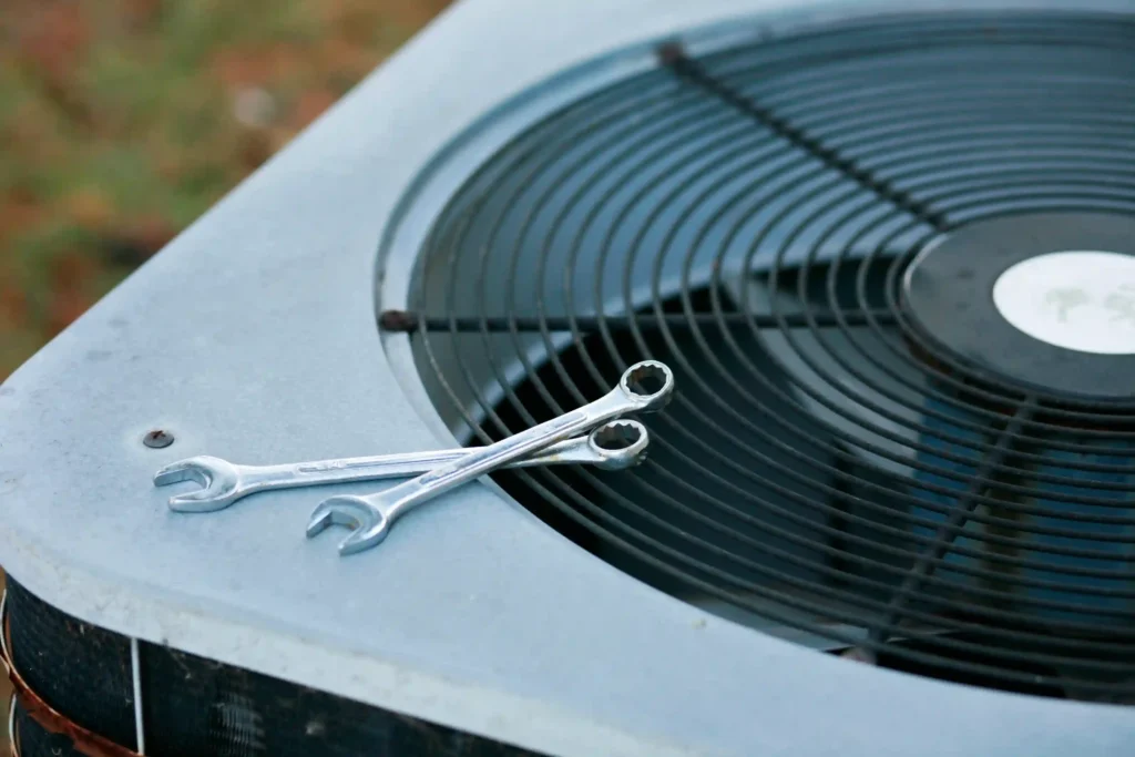 A close-up shot of two wrenches resting on the top of an outdoor air conditioner unit.