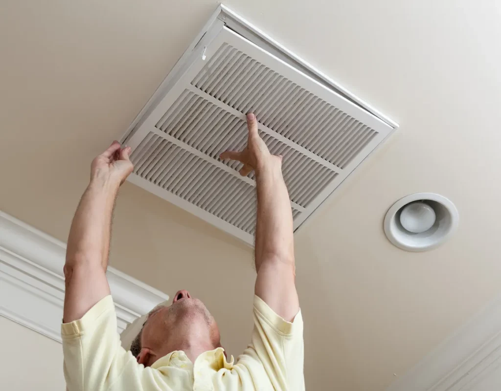 A person installs a square air filter into a ceiling vent